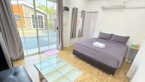 A modern bedroom with a bed, a glass-top table, a bench, and a view of the outside. - Cina Home (Chiang Mai)