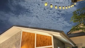 A building with a modern design, featuring a large wooden panel on the facade and a string of lights against a cloudy sky. - Cina Home (Chiang Mai)