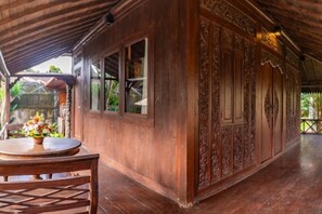 A wooden building with intricate carvings, a table with a floral centerpiece, and a covered area with a wooden ceiling. - Villa Lestaru Ubud (Bali)