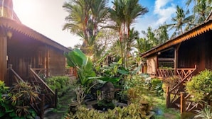 A tropical garden with a stone pathway, a small pond, and a wooden structure with a balcony. - Villa Lestaru Ubud (Bali)