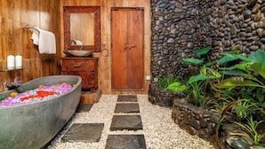 A bathroom with a large bathtub, wooden walls, a stone wall, and a small garden area. - Villa Lestaru Ubud (Bali)