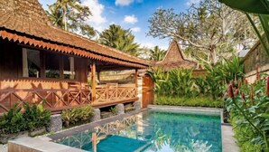A pool area with a wooden deck, a thatched-roof structure, and lush greenery. - Villa Lestaru Ubud (Bali)