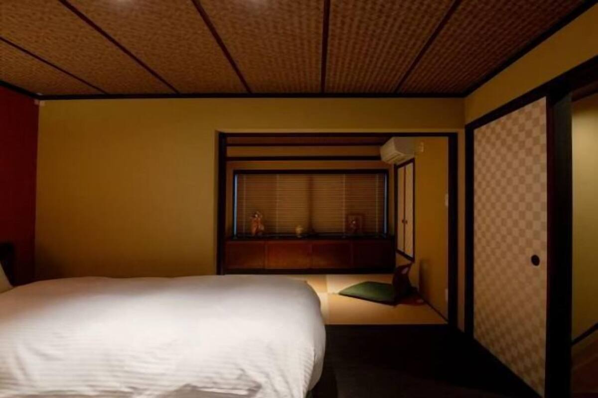 A hotel room with a bed, a window with blinds, a small seating area, and a sliding door.