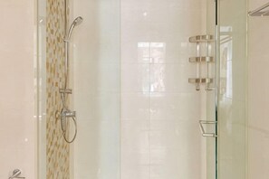 Una ducha con cerramiento de vidrio, pared con azulejos, un cabezal de ducha y puerta de vidrio.