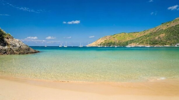 A beach with clear water, distant sailboats, and a hilly landscape. - Rawai Beach Pool Condotel (Phuket)