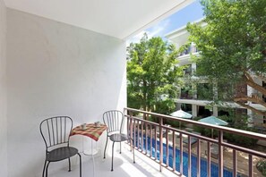 A balcony with a table and chairs, overlooking a swimming pool and greenery. - Rawai Beach Pool Condotel (Phuket)