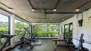 A gym with exercise equipment, large windows, and a view of greenery. - Rawai Beach Pool Condotel (Phuket)