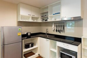 Une cuisine compacte avec des meubles blancs, un réfrigérateur en acier inoxydable, un plan de travail noir et un four encastré.