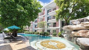 A swimming pool with a circular mosaic design, surrounded by lounge chairs and umbrellas, with a building in the background. - Rawai Beach Pool Condotel (Phuket)