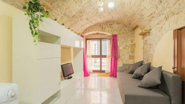 Een gezellige woonkamer met een stenen plafond, een grijze bank, een flatscreen-tv en een witte kast.