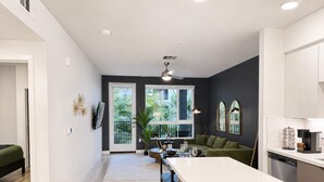 Eine moderne Küche mit einer zentralen Kochinsel, ein Essbereich mit einem grünen Sofa und Blick auf Grünflächen.