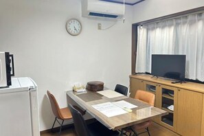 A room with a wooden table, chairs, a clock, a television, and a window with curtains. - HAMANOCHO BEEKAN (Takamatsu)