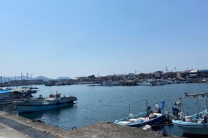 A harbor with boats docked, a clear sky, and a distant town. - HAMANOCHO BEEKAN (Takamatsu)