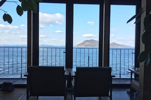 A room with a view of the sea and a mountain, featuring two chairs and a table.