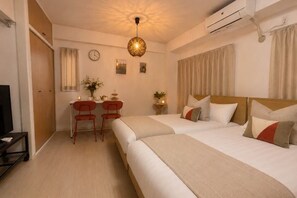 A hotel room with two beds, a desk with chairs, a TV, and a ceiling light fixture.