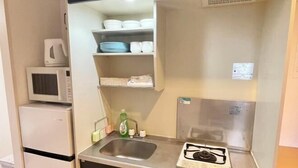 A compact kitchenette with a microwave, sink, and gas stove. - YMK Oshiage 5B (Tokyo)