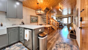 Una cocina moderna con armarios grises, un refrigerador de acero inoxidable y una escalera de madera que lleva a una sala de estar.