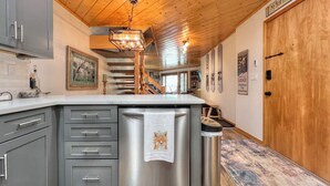 Una cocina con armarios grises, un refrigerador de acero inoxidable, techo de madera y una escalera que lleva a un altillo.
