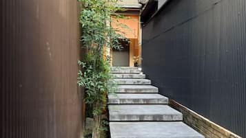A narrow concrete staircase leading to a door, surrounded by a wooden fence and vegetation.