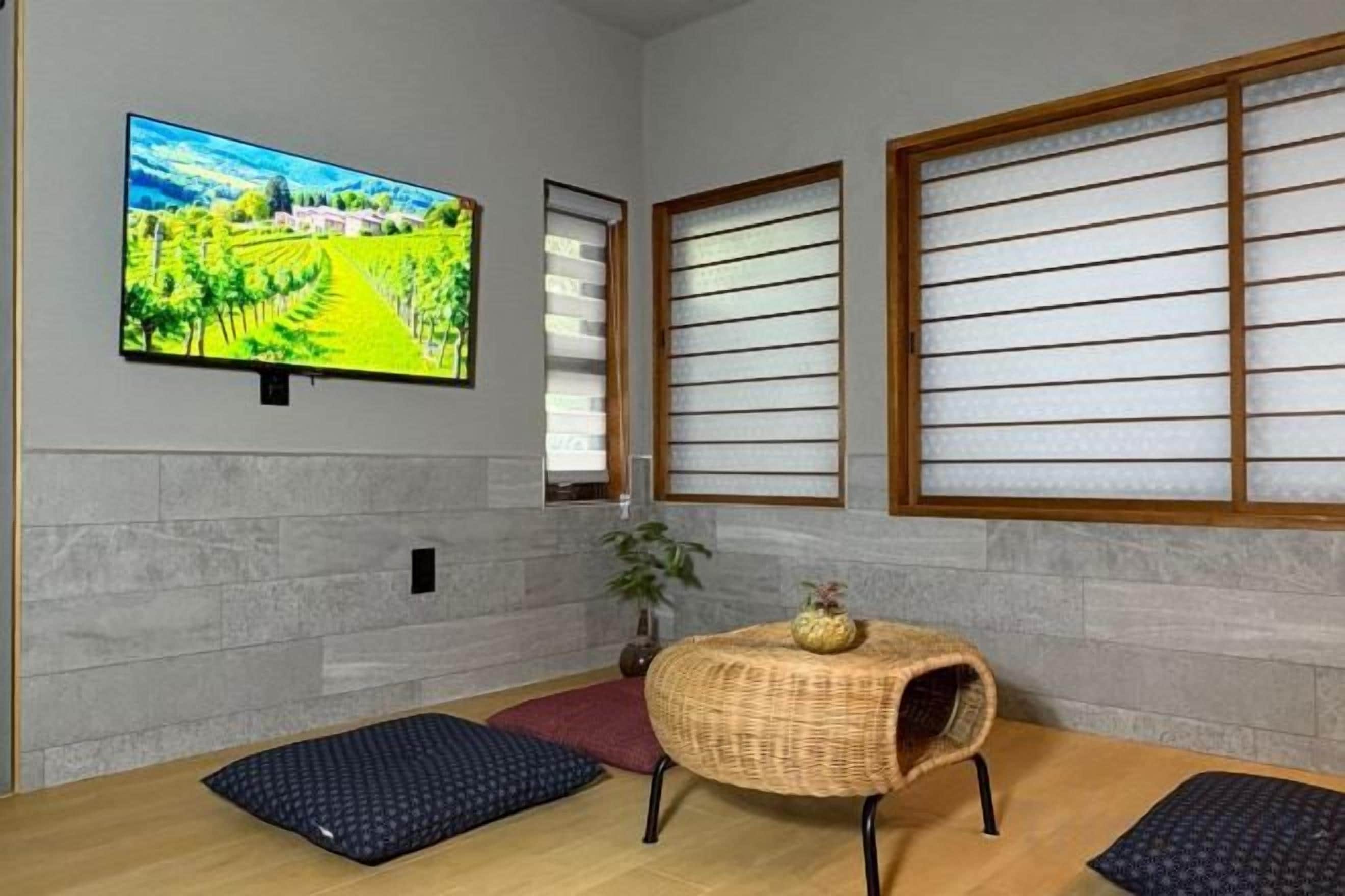 A room with a television, tatami mats, a woven table, and shoji screens.