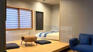 A modern hotel room with a bed, a blue sofa, a small table with a lamp, and a window with blinds. - SOSEI-IN@YASAKA TEMPLE (Kyoto)