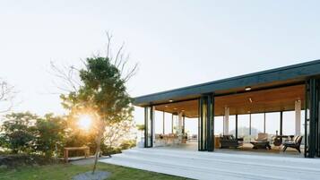 Une maison moderne dotée d’un patio couvert, de grandes fenêtres et d’un arbre au premier plan.