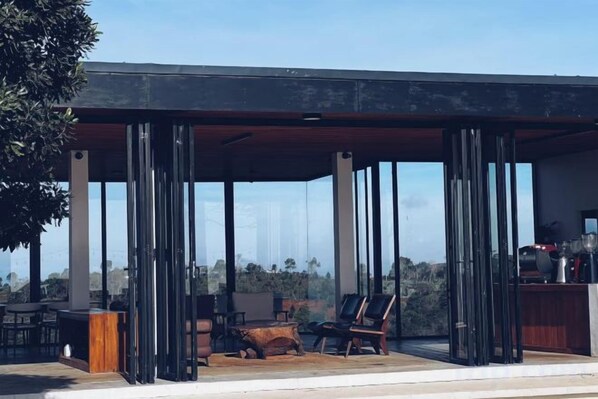 A covered outdoor seating area with chairs and a table, large windows, and a view of the landscape.