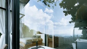 A modern bedroom with a glass wall, a bed, and a bathroom with a bathtub.