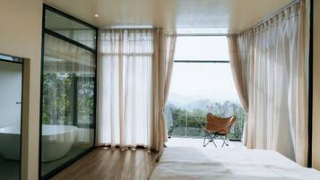 A modern bedroom with a large bed, a glass-enclosed bathroom, and a view of the outdoors.