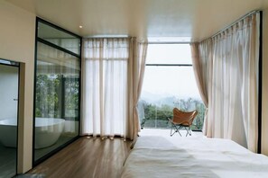 A modern bedroom with a large bed, a glass-enclosed bathroom, and a view of the outdoors.