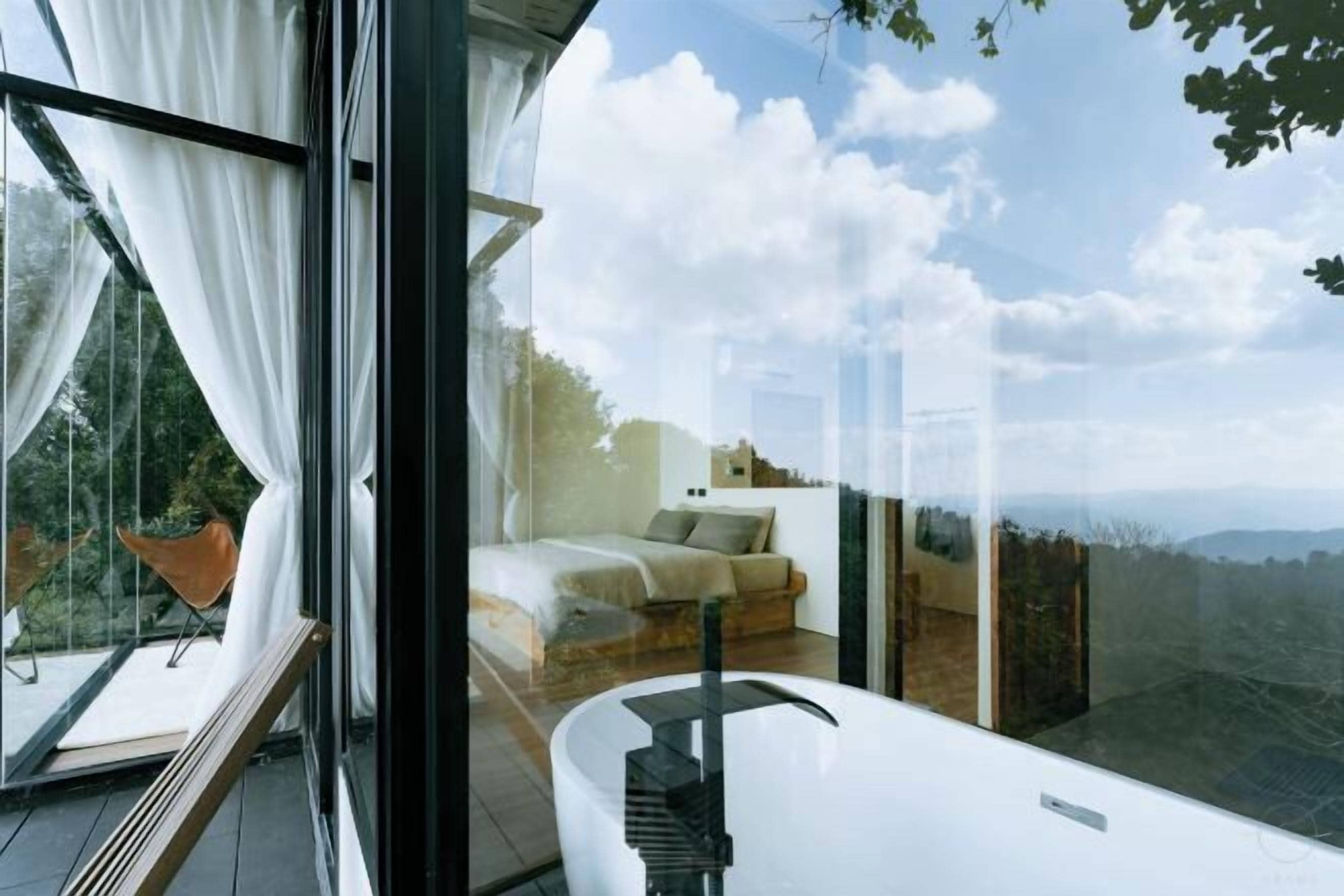 A modern bedroom with a large window, a white bathtub, and a view of the outdoors.