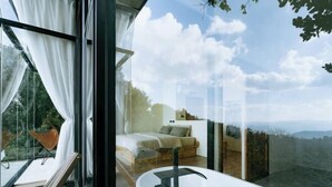 A modern bedroom with a large window, a white bathtub, and a view of the outdoors.