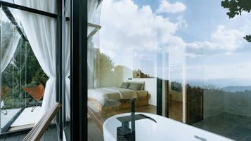 A modern bedroom with a large window, a white bathtub, and a view of the outdoors.