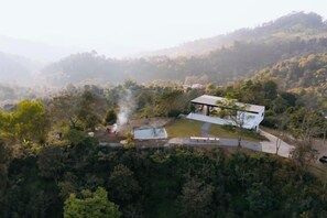 Un edificio moderno con techo plano y un espacio exterior cubierto, rodeado de un bosque denso.