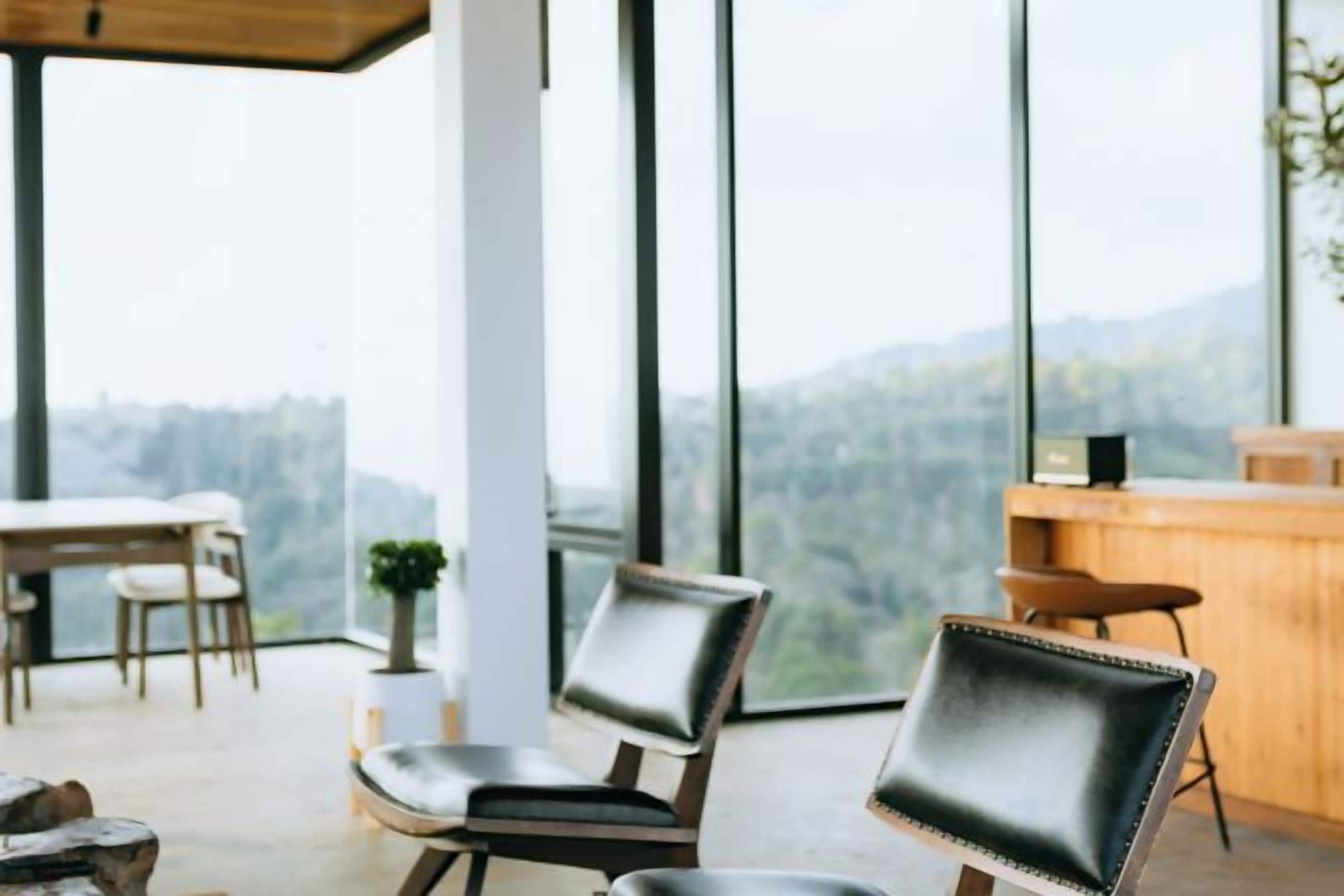 A modern interior with a dining area, two leather chairs, a wooden table, and a view of the outdoors.
