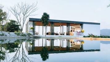 Una casa moderna con fachada de vidrio, piscina y el reflejo de la casa.