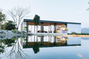 A modern house with a glass facade, a pool, and a reflection of the house. - Akano Doichang (Mae Suai)