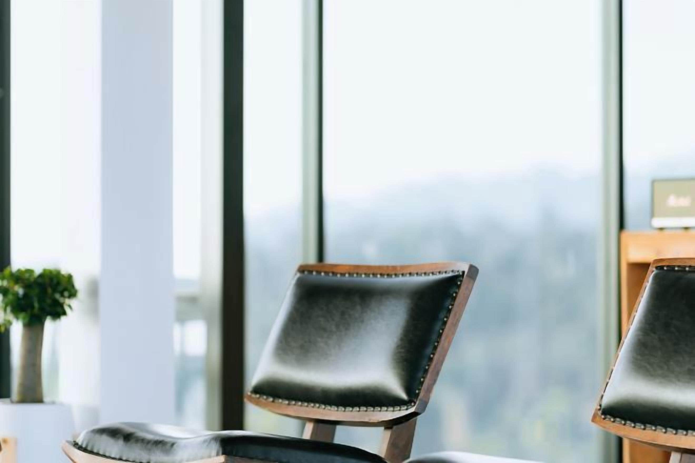 A chair with a cushioned backrest and wooden frame, positioned in front of a window with a view of a cityscape.
