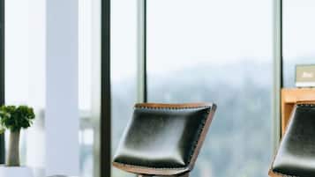 A chair with a cushioned backrest and wooden frame, positioned in front of a window with a view of a cityscape.