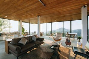 A spacious living area with a wooden ceiling, large windows, and a view of the outdoors. - Akano Doichang (Mae Suai)
