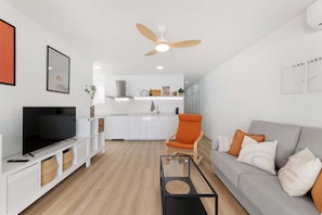A modern living room with a flat-screen TV, a grey sofa, an orange armchair, and a ceiling fan.