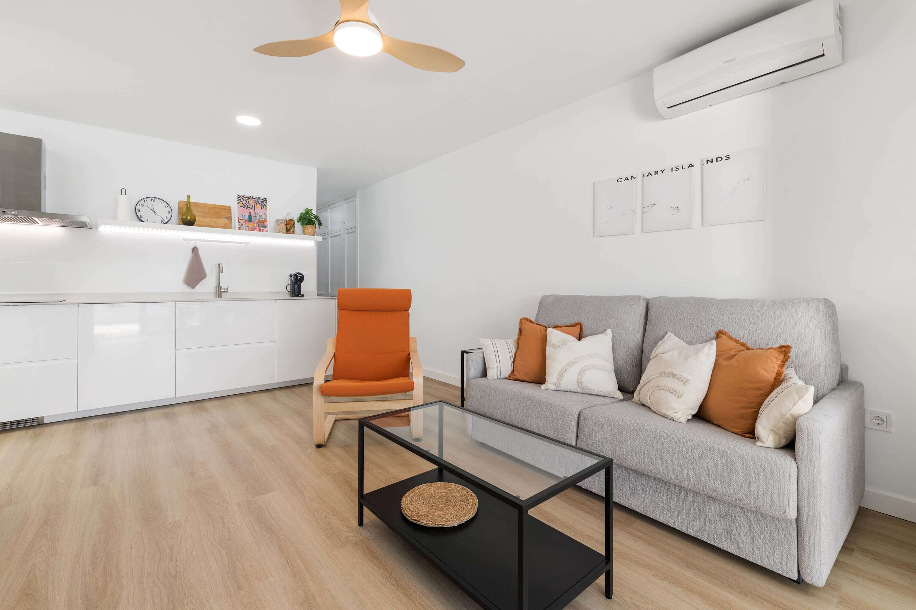 Una sala de estar moderna con un sofá gris, un sillón naranja y una mesa de centro de vidrio.