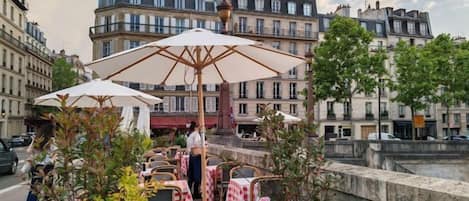 Outdoor seating with umbrellas, a stone wall, and buildings in the background.