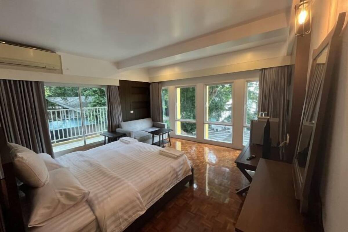 A hotel room with a bed, a desk, a chair, and large windows.