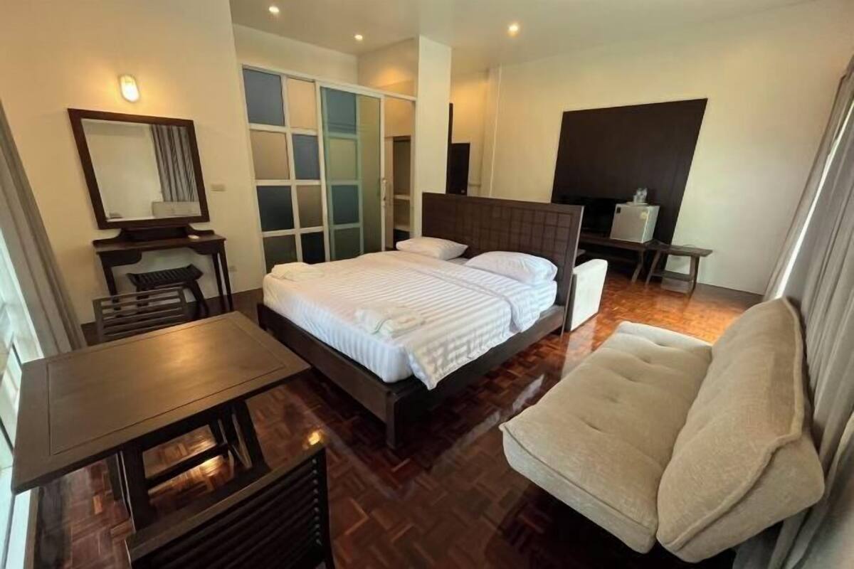 A modern hotel room with a large bed, a desk, a chair, a sofa, and a TV.