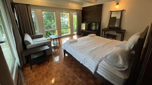 A hotel room with a bed, a sofa, a TV, a desk, and large windows with curtains. - Molecular cloud (Pattaya)