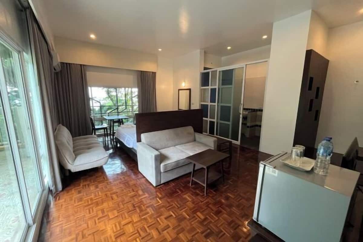Ein Hotelzimmer mit Holzboden, einer Couch, einem kleinen Tisch, einem Kühlschrank und einer Schiebetür zu einem Balkon.