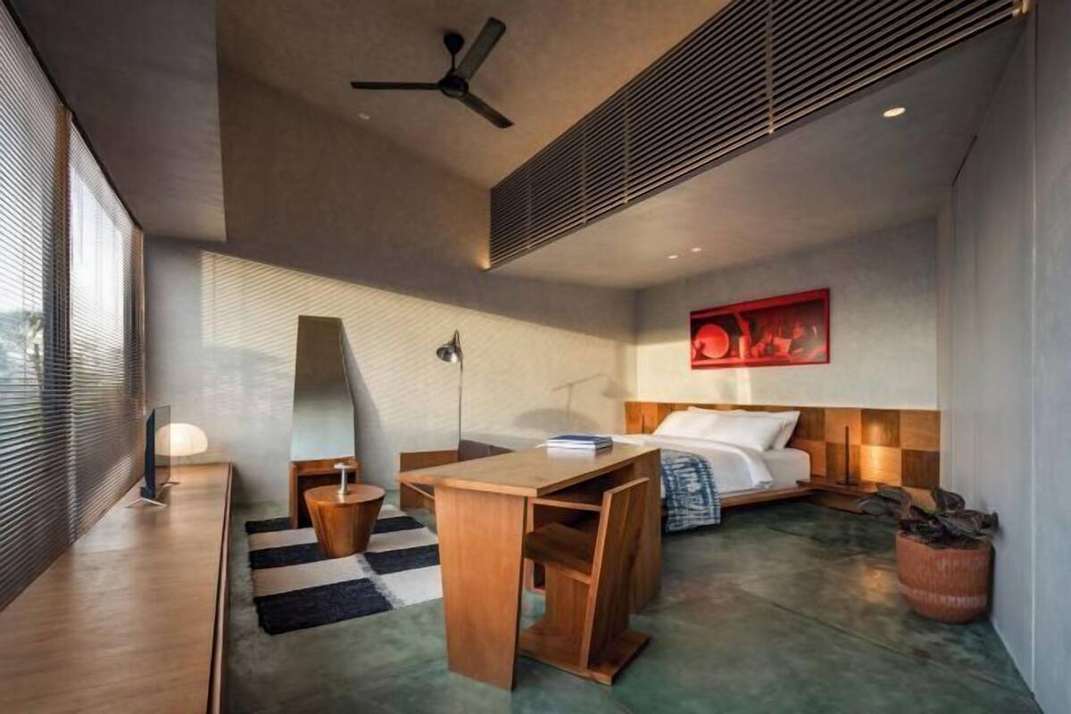 A modern hotel room with a bed, desk, and chair, a ceiling fan, and a large window.