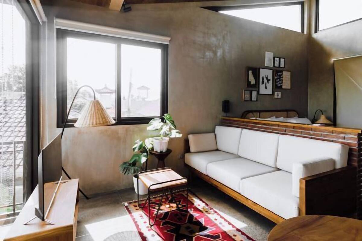 A modern living room with a white sofa, a small table, a potted plant, and a large window.