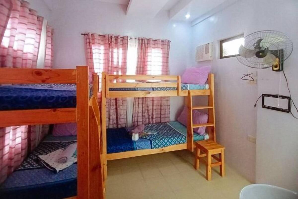 Habitación con literas, una escalera de madera, una mesita y un ventilador en la pared.